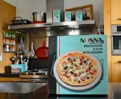 Nonna Pizzasteen Ø30,5 Met RVS Serveerrek - Stenen Pizzaplaat / Ovenplaat (11mm Dik) Voor Oven En Barbecue (BBQ) - Maximaal 600 Graden Celcius -Barbecue Benodigdheden 1200x985